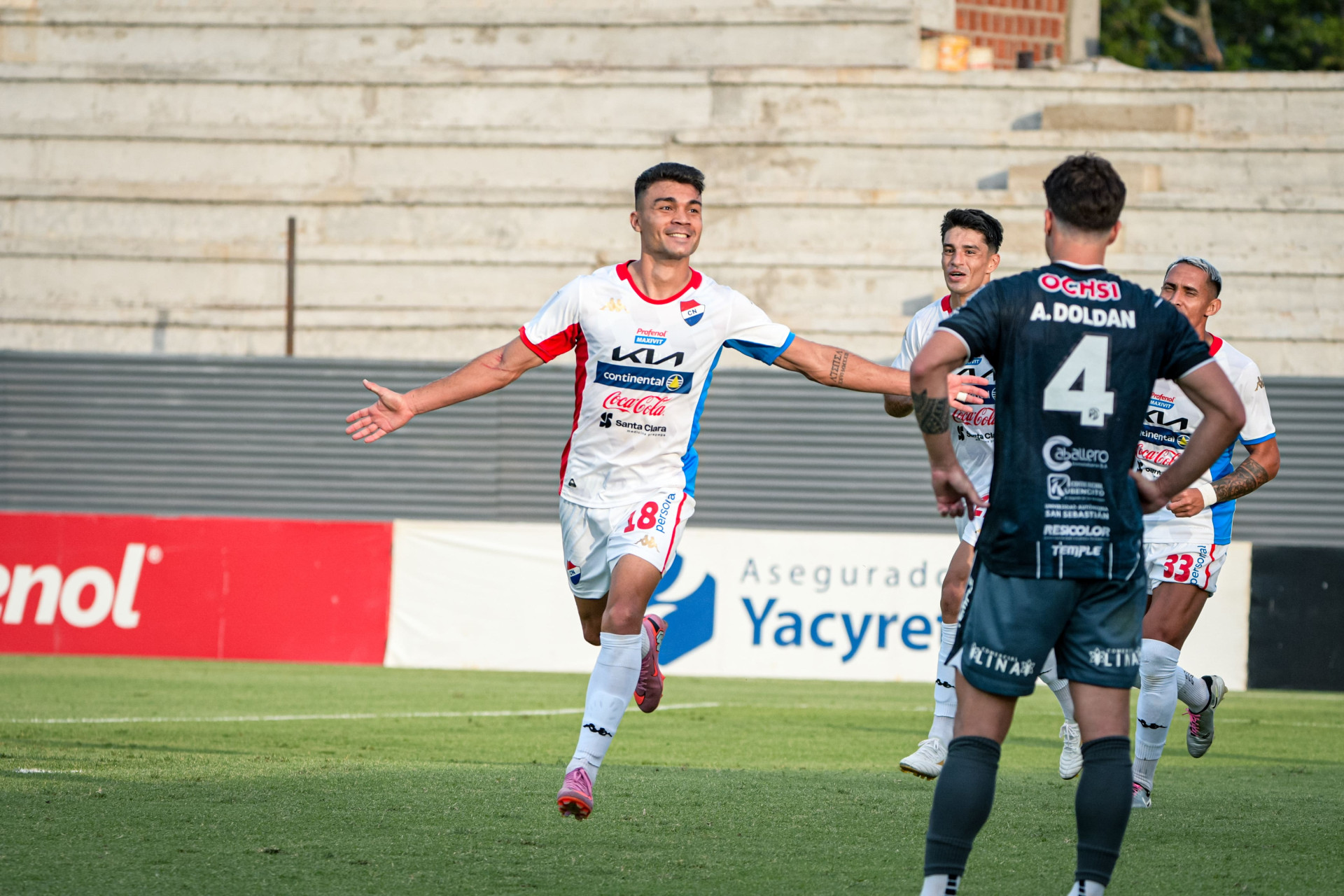 Un jugador de Nacional celebra un gol con los brazos abiertos junto a compañeros, ante un rival